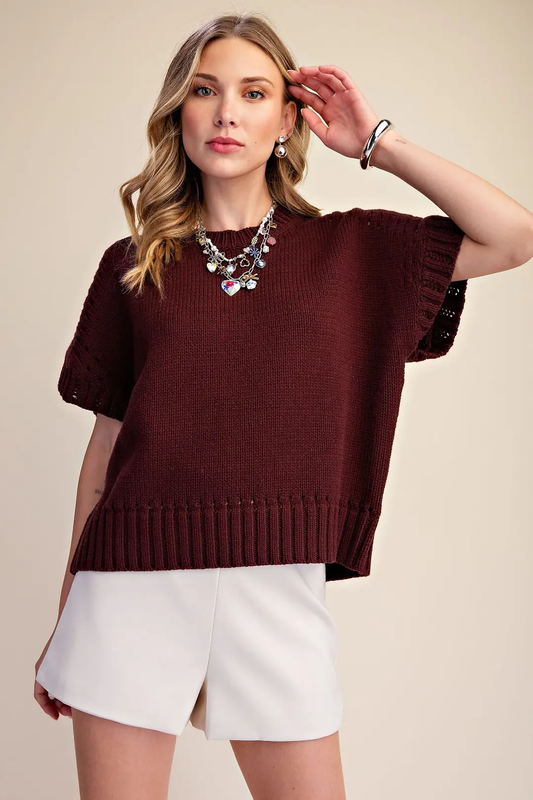Model wearing a dark burgundy short-sleeve crew-neck sweater with eyelet sleeve accents and a ribbed hem