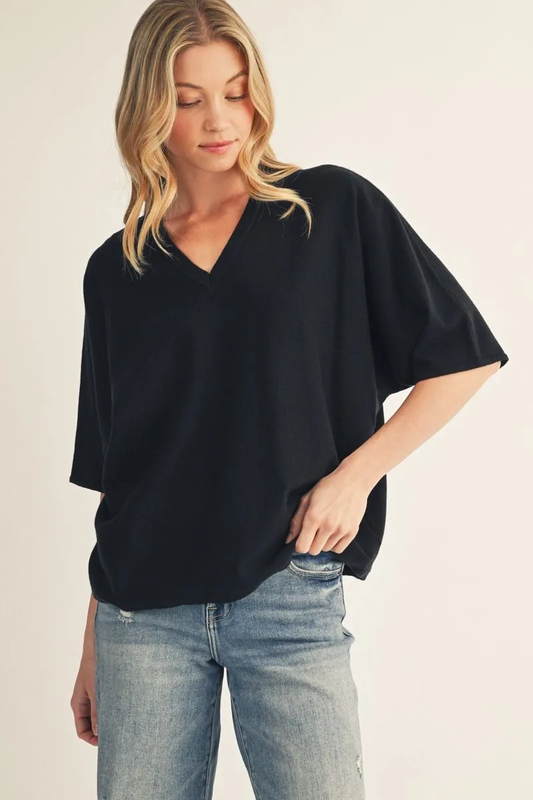 Model wearing a black lightweight drop-shoulder V-neck sweater top with short sleeves, styled with denim