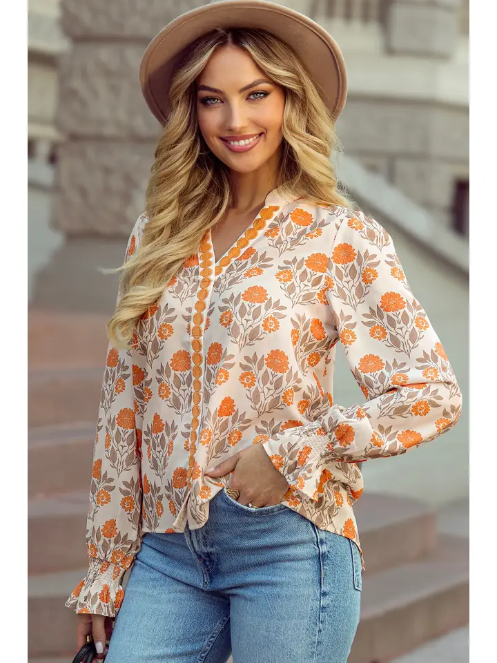 Model wearing a cream V-neck long-sleeve blouse with orange flowers and muted leafy details